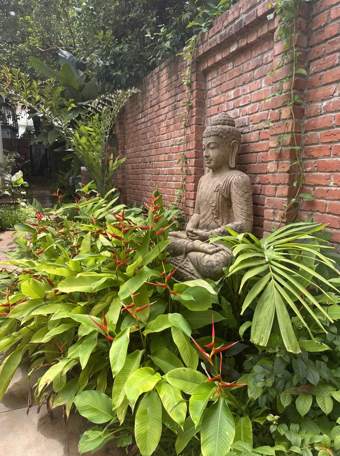 Contemplative corner — Heliconia, monstera and stone sculpture against brick